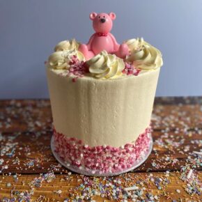 Tall Buttercream Cake with a Pink teddy Topper and Pink Sprinkles around the bottom of the cake